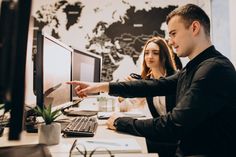 two people are sitting at a desk and pointing to the computer screen that is on