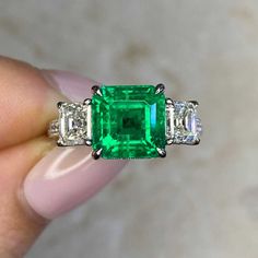 an emerald and diamond ring is being held in someone's hand with three diamonds around it