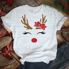 a white t - shirt with reindeer's face and red bow on it, sitting next to pine cones