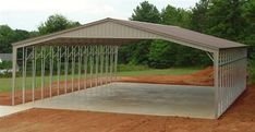 a metal carport sitting in the middle of a dirt field next to some trees