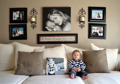 a baby sitting on top of a white couch in front of some framed pictures and photos