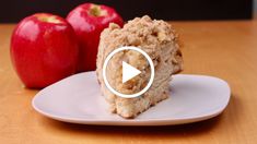 a piece of cake sitting on top of a white plate next to two red apples