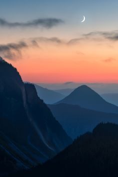 the sun is setting over some mountains with trees on it and a crescent in the sky