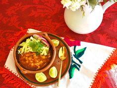 a bowl of chili with limes and cilantro on a red tablecloth