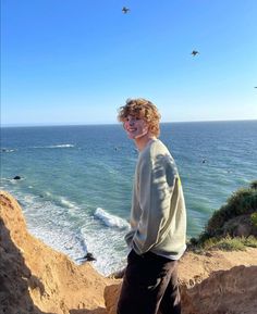 a young man standing on top of a cliff next to the ocean