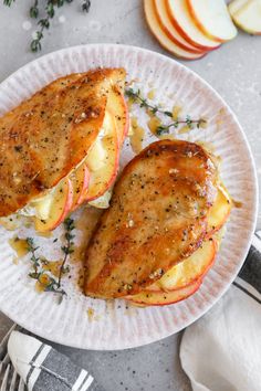 two pieces of chicken with apple slices on a paper plate next to silverware and napkins