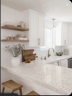 a white kitchen with marble counter tops and open shelving above the sink, along with wooden stools