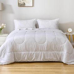 a bed with white comforter and pillows in a small room next to a nightstand