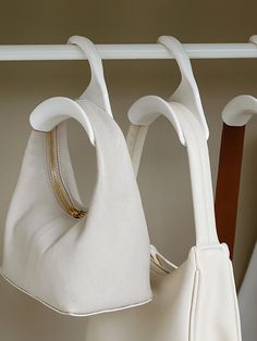 two white purses hanging on hooks in a closet