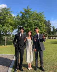 two men and a woman posing for a photo in front of some trees with their hands up