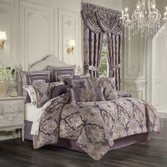 a bed with purple and white comforters in a room next to a chandelier