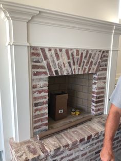 a man standing next to a brick fireplace with a box on it's mantle