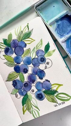 a watercolor painting with blueberries and green leaves on it, next to a paintbrush