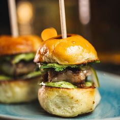 two hamburgers with toothpicks in them sitting on a blue plate, ready to be eaten