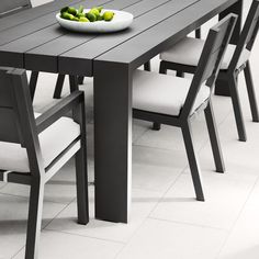 a dining table with white chairs and a bowl of green fruit on top of it