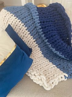 a blue and white crocheted blanket sitting on top of a couch next to pillows