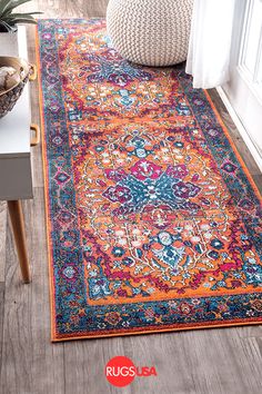 an orange and blue rug on the floor in front of a white wall with a plant