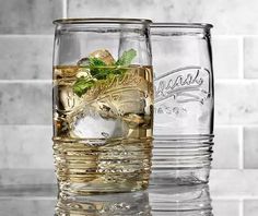 two glasses filled with ice and mint sitting on top of a glass table next to each other