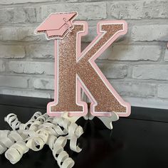 a pink and gold glitter letter k on a black table