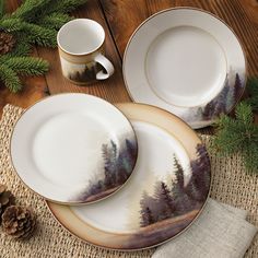 two white plates with trees painted on them next to pine cones and evergreen branches,