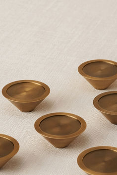 six brown bowls sitting on top of a white cloth covered table next to each other