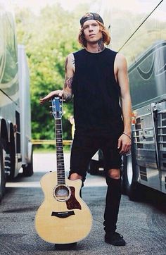 a man standing next to a bus holding a guitar