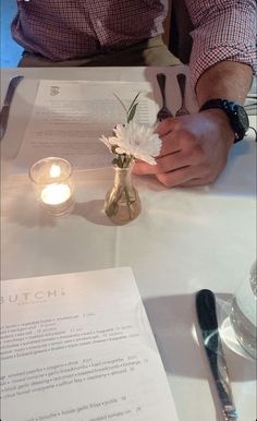 a man sitting at a table with flowers in a vase next to an open book