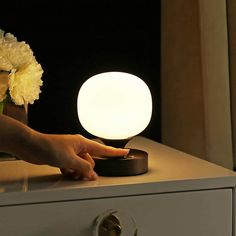 a person's hand reaching for a light on top of a dresser next to flowers