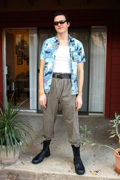 a man standing in front of a red building wearing sunglasses and a blue hawaiian shirt