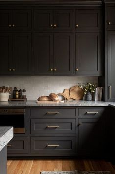 a kitchen with black cabinets and gold handles on the counter tops, along with a wooden floor