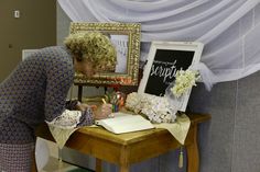 a woman writing on a notepad in front of a desk with a mirror and flowers