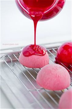 pink and red doughnuts on cooling rack with sauce pouring over them to make it look like they are melting