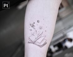 an open book tattoo on the left inner forearm and arm, with flying flowers coming out of it