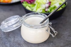 a glass jar filled with yogurt next to a bowl of salad