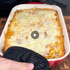 a person holding a spatula in front of a casserole dish with cheese