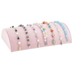 six bracelets are lined up on a pink velvet bag, each with different colored beads and charms