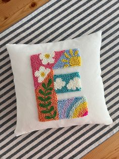 a decorative pillow with the letter e made out of beadwork on it sitting on a striped tablecloth