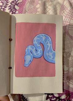 an open book with a drawing of a blue snake on it's cover and pink background