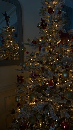 a white christmas tree with red and gold ornaments on it's branches in front of a mirror