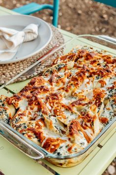 a casserole dish with cheese and spinach is on a table next to a plate