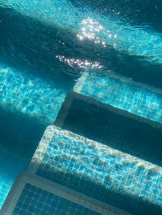 an overhead view of a swimming pool with blue water and sun reflecting off the tiles