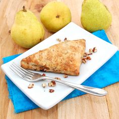 a white plate topped with food next to two pears and a fork on top of a wooden table