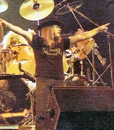 a man with long hair playing drums in front of other drummers on stage at a concert