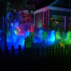 a group of tombstones lit up at night in front of a house with blue and green lights