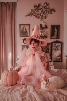 a woman in a pink dress and hat sitting on a bed next to a cat