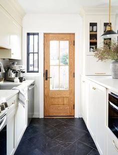 a kitchen with white cabinets and black tile flooring next to a wooden front door