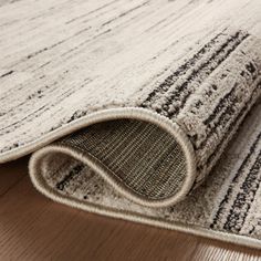 an area rug on the floor with a wooden floor and white walls in the background