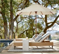 an outdoor lounge chair and umbrella next to a swimming pool with trees in the background