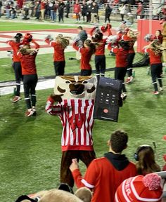 a group of people standing on top of a field with mascot costumed in red and white