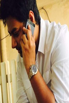 a man talking on a cell phone while holding his hand up to his ear and wearing a watch